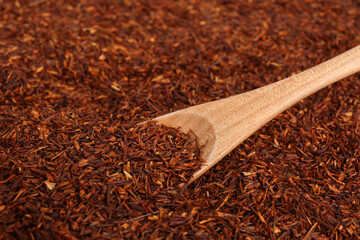 Heap of dry rooibos tea leaves with wooden spoon, closeup view