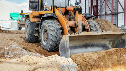 Obraz premium A powerful front loader on the construction site performs sanding. Moving soil with construction equipment. Excavation.