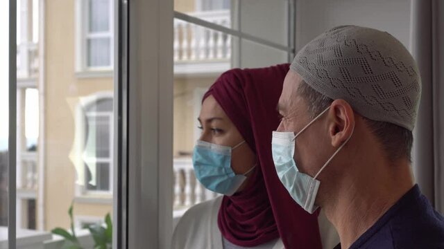 Sad Arabic Muslim family couple man and woman in protective medical masks. Home self-isolation, quarantine, lockdown. COVID-19 pandemic. Muslim refugees and displaced people. European migrant crisis