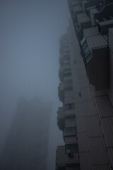 Two tall residential buildings in the form of a tower, immersed in a misty gray sky. Cyberpunk stylistics. Dramatic, depressing mood.