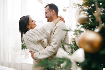 Young couple hugging near Christmas tree at home