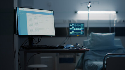 Hospital ward with empty bed and modern equipment at medical facility unit. Nobody in emergency room with files information computer, heart rate monitor, stethoscope and technology
