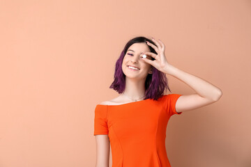 Young woman with purple hair holding chewing gum on beige background