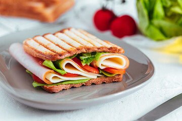 Toast sandwich with gouda cheese and turkey ham filled with tomato and lettuce on a bright background with ingredients in blurry background