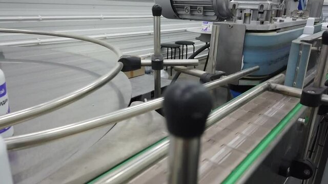 Two white antiseptic plastic bottles on metallic conveyor glued labels approaching to camera