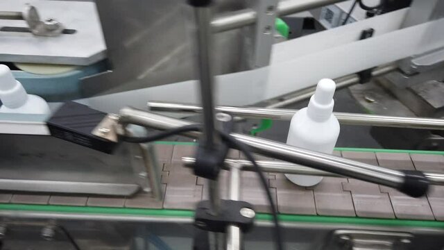 White antiseptic plastic bottles on metallic conveyor gluing labels, camera following one bottle