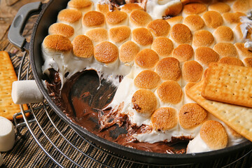Frying pan with tasty S'mores dip and crackers on wooden table, closeup