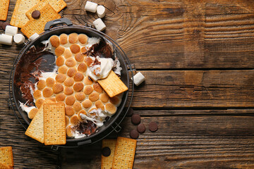 Frying pan with tasty S'mores dip and crackers on wooden background - obrazy, fototapety, plakaty