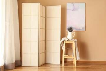 Vase with lavender flowers on stool and folding screen near beige wall