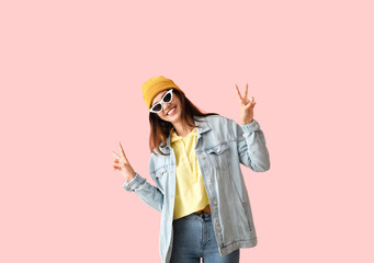 Cool young woman showing victory gesture on color background