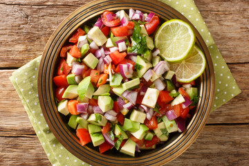Tasty Kachumbari is a popular East African salad made with tomatoes, onion and avocado close up in the plate on the table. Horizontal top view from above