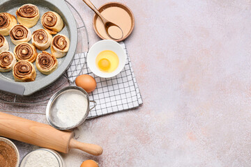 Baking dish of uncooked cinnamon rolls and ingredients on light background, closeup