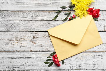 Envelope and beautiful flowers on light wooden background
