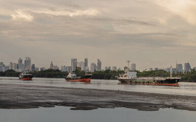 Bangkok, Thailand - 31 Jul 2021 : Three cargo ship parked in the middle of the Chao phraya river on evening skyscraper background. No focus, specifically.