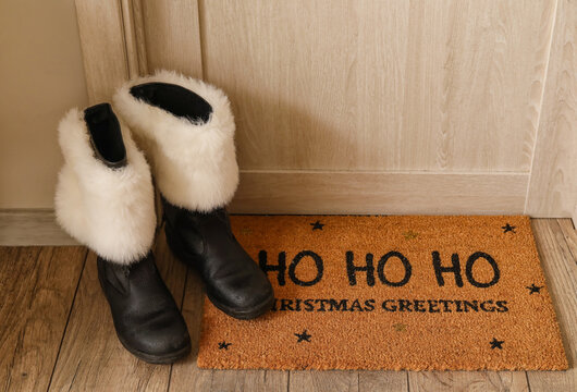 Santa boots and floor mat with Christmas greetings near door in room