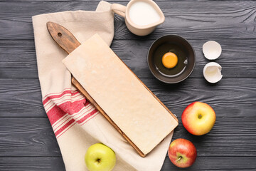 Board with fresh dough and ingredients for apple strudel on black wooden background