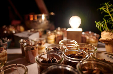 Fototapeta na wymiar Mousse au chocolat in kleinen geöffneten Gläsern stehen in Reihe auf einem Buffettisch vor einer eingeschalteten Glühbirne auf einer Veranstaltung