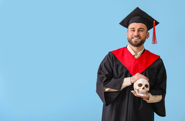 Handsome male graduate with human skull on blue background