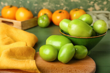Board and bowl with fresh green tomatoes on table