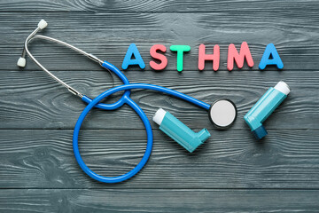 Asthma inhalers, stethoscope and word ASTHMA on dark wooden background