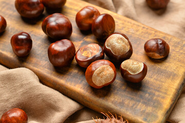Wooden board with chestnuts on fabric background, closeup