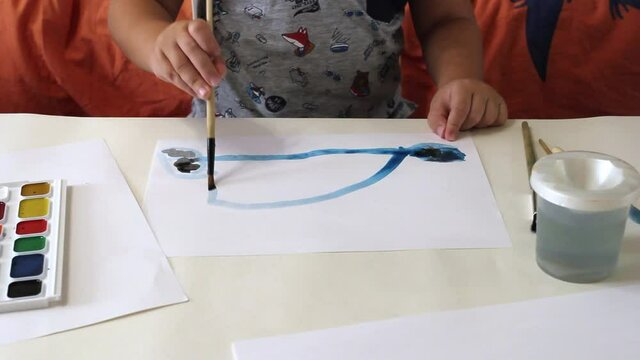 child draws with paints on a white sheet