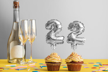 Tasty Birthday cupcakes with champagne on grey background