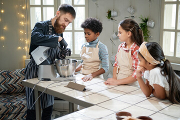 Chef showing the work of mixer to children during cooking lesson in the kitchen