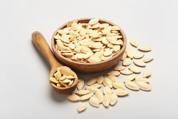 Bowl and spoon with natural pumpkin seeds on light background