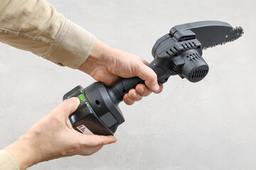 Finger presses battery charge check button for a portable chain saw, charge indicators are shown,...