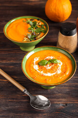 Bowls with tasty pumpkin cream soup on wooden background