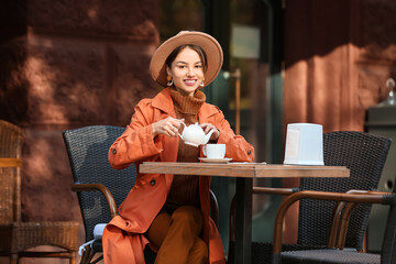 Beautiful young woman pouring tea from teapot in street cafe