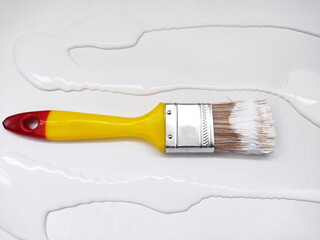 Paint brush with yellow handle and white paint on canvas. Preparing for background priming. Painting brush with paint on stiff bristles. close-up photography.
