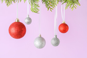 Different Christmas balls hanging on thuja branches against lilac background, closeup