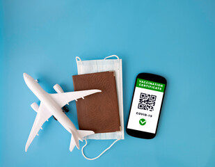 A phone with an electronic covid 19 vaccination certificate, a passport mask and a model airplane on a blue background.