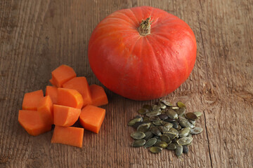 Red kuri squash and a bunch of peeled seeds on a rough woody texture background. Selective focus.