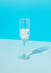 Modern New Year scene with champagne glass, snowflakes and sunny shadows on table against blue background. Creative luxury xmas party. Minimalism