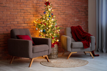 Beautiful Christmas tree with glowing lights and armchairs near brick wall