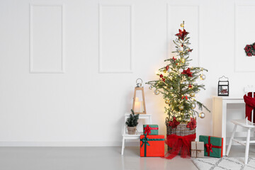 Christmas tree with gifts, candles and stepladder near light wall