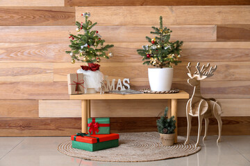 Bench with small Christmas trees, gifts and reindeer near wooden wall