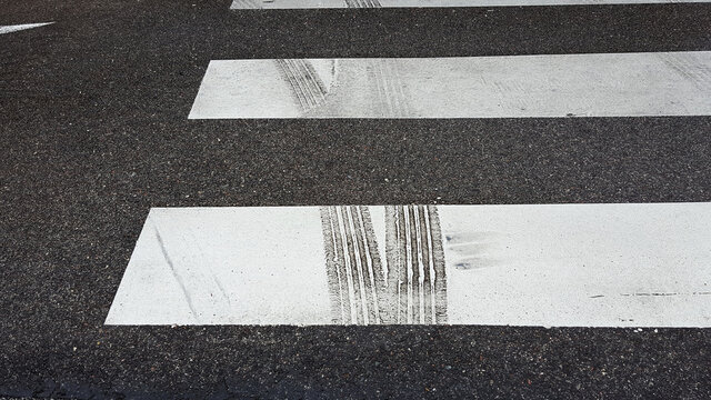 closeup view of white painted zebra pedestrian crossing with prominent black coloured car tyre marks