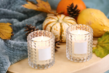 Burning candles in holders and autumn decor on sofa
