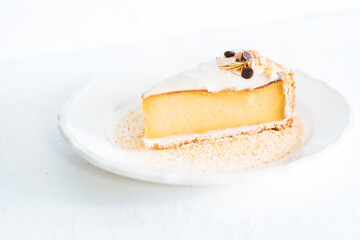 French flan on white plate with biscuit crumbs around, with almonds on top. Piece of cake on white bright background, traditional french  dessert