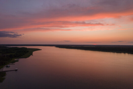 Aerial landscape of the lake surrounded by the green forest. Pastel orange clouds during summer sunset. © Jakub Łukasik