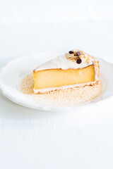 French flan on white plate with biscuit crumbs around, with almonds on top. Piece of cake on white bright background, traditional french  dessert