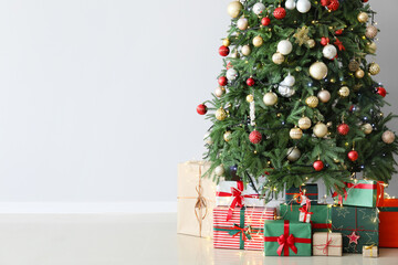 Fototapeta na wymiar Christmas tree and gift boxes near light wall