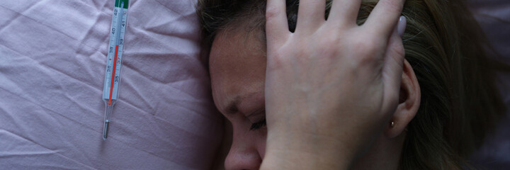 Young woman in bed and holding her head near mercury thermometer