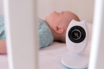 Baby monitor camera watching over a Caucasian baby while he sleeps in the crib.