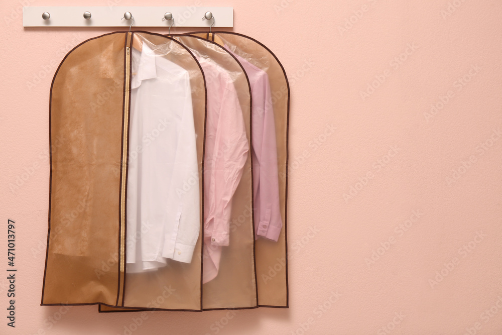 Wall mural Garment bags with clothes hanging on light wall. Space for text - Wall murals