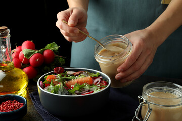 Concept of cooking vegetable salad with tahini sauce on dark textured table